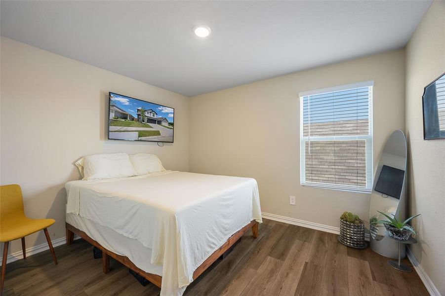 Bedroom featuring wood-finish flooring, recessed ceiling lighting, and a single window with blinds Bedroom featuring wood-finish flooring, recessed ceiling lighting, and a single window with blinds