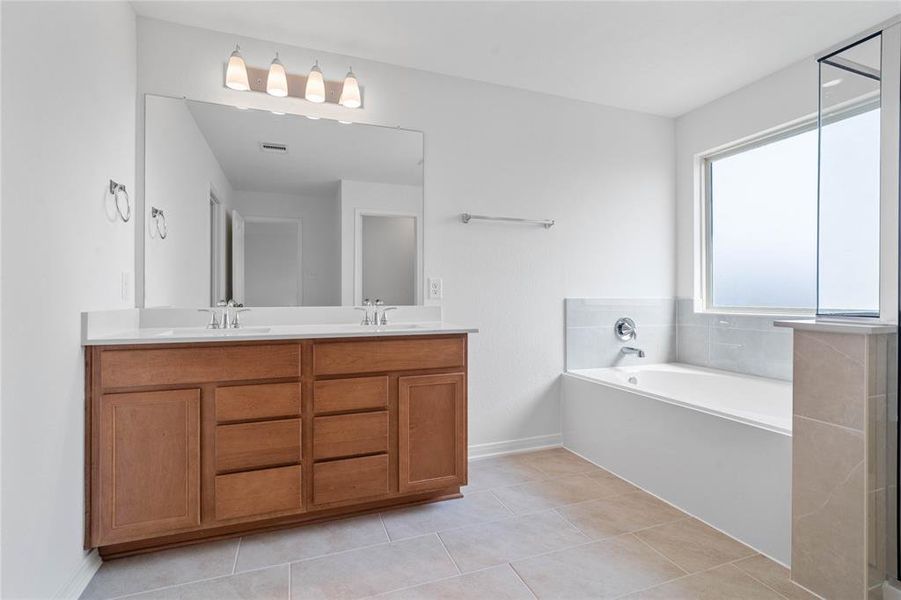 This primary bathroom is definitely move-in ready! Featuring an oversized tub and walk-in shower with tile surround, stained cabinets with light countertops, dual vanities, high ceilings, neutral paint, sleek and modern finishes.