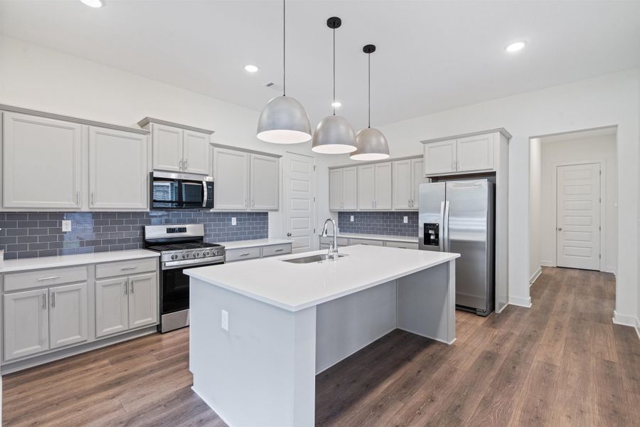 Kitchen with stainless steel appliances, a center island with sink, dark wood finished floors, decorative light fixtures, and backsplash