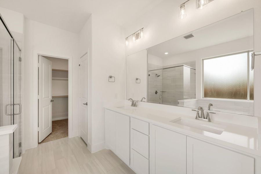 Master bathroom with double vanity, white cabinets, glass shower, and walk-in closet entrance