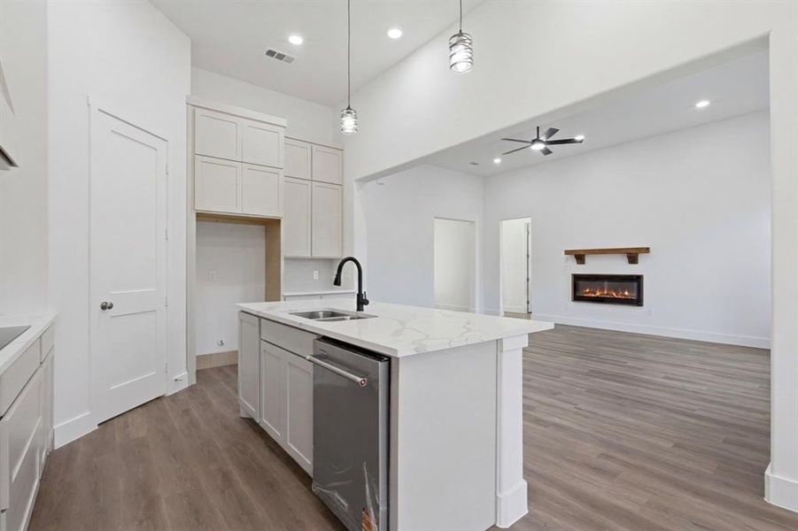 Open-concept kitchen featuring a central island with a sink, stainless steel dishwasher, and quartz countertop