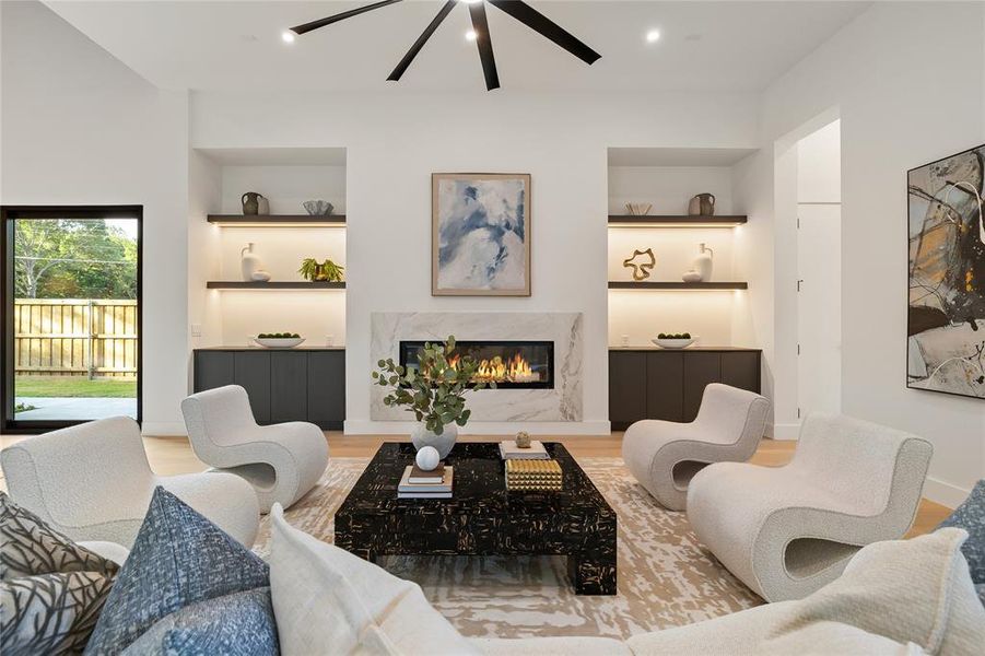 Living space featuring a linear gas fireplace with a stone surround, integrated built-in shelving with accent lighting, dark built-in cabinetry, and wood-finish flooring Living space featuring a linear gas fireplace with a stone surround, integrated built-in shelving with accent lighting, dark built-in cabinetry, and wood-finish flooring