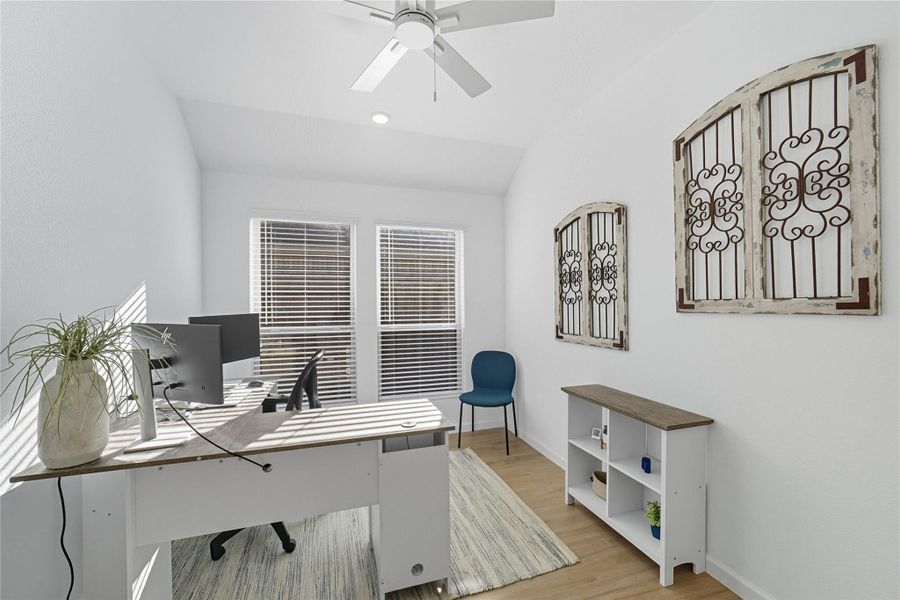 Bright and cozy home office with a large window, featuring light wood flooring and a ceiling fan. Bright and cozy home office with a large window, featuring light wood flooring and a ceiling fan.