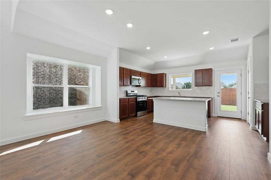 Kitchen featuring appliances with stainless steel finishes, decorative backsplash, recessed lighting, dark wood finished floors, and a center island