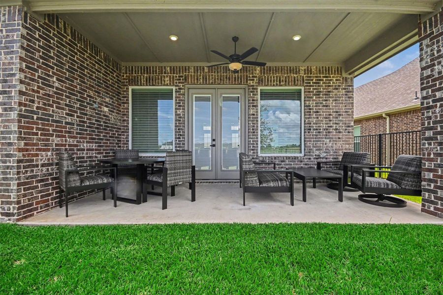 A cozy covered patio with brick walls, featuring outdoor seating and a ceiling fan, overlooks a lush green lawn. Ideal for relaxing and entertaining. A cozy covered patio with brick walls, featuring outdoor seating and a ceiling fan, overlooks a lush green lawn. Ideal for relaxing and entertaining.