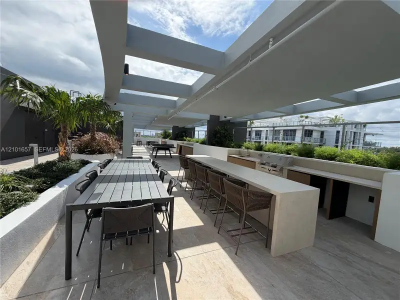 Rooftop terrace featuring a stone-topped built-in bar, integrated stainless steel grill, overhead pergola structure, and tiered concrete planters