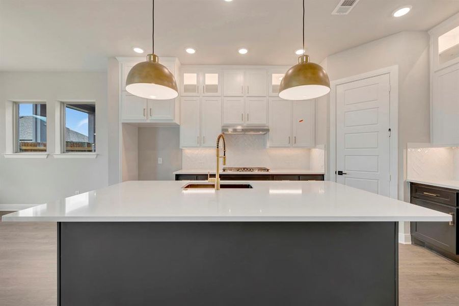 Kitchen featuring glass insert cabinets, backsplash, two tone color scheme, and pendant lighting