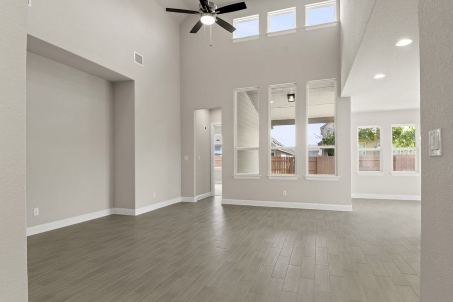 A living room room with vinyl flooring, white-framed windows, and white painted walls.