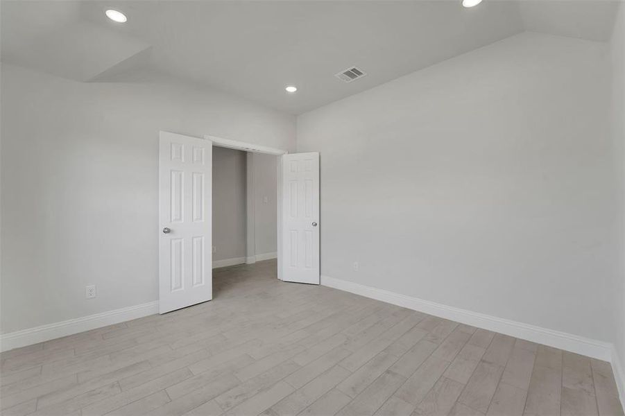 Unfurnished bedroom featuring light wood finished floors, baseboards, visible vents, and vaulted ceiling Unfurnished bedroom featuring light wood finished floors, baseboards, visible vents, and vaulted ceiling
