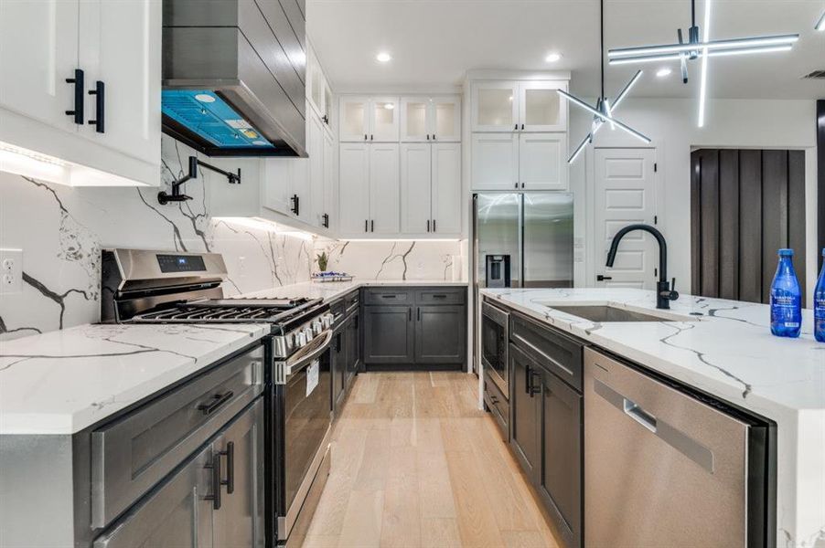 Kitchen featuring light stone countertops, stainless steel appliances, light wood-style floors, white cabinets, and custom exhaust hood Kitchen featuring light stone countertops, stainless steel appliances, light wood-style floors, white cabinets, and custom exhaust hood