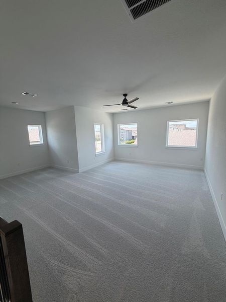A spacious room offers comfortable carpeted flooring and multiple windows for abundant natural illumination.