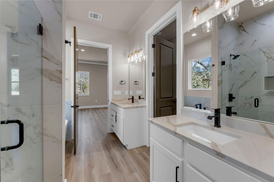 Full bathroom featuring a marble finish shower, two vanities, and light wood-style flooring