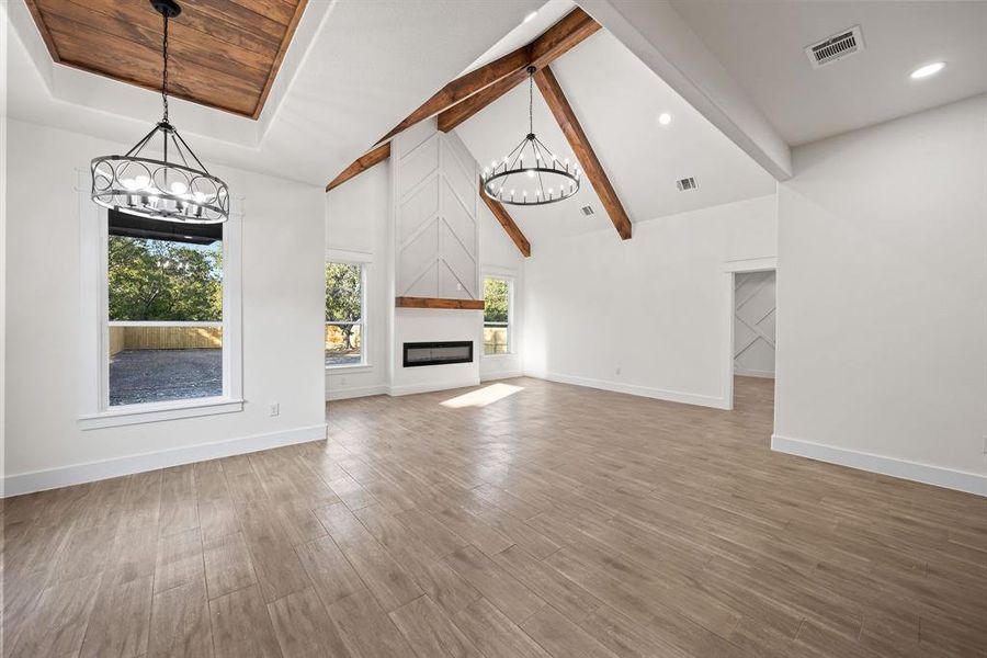 Unfurnished living room featuring a chandelier, beamed ceiling, wood finished floors, a fireplace, and high vaulted ceiling