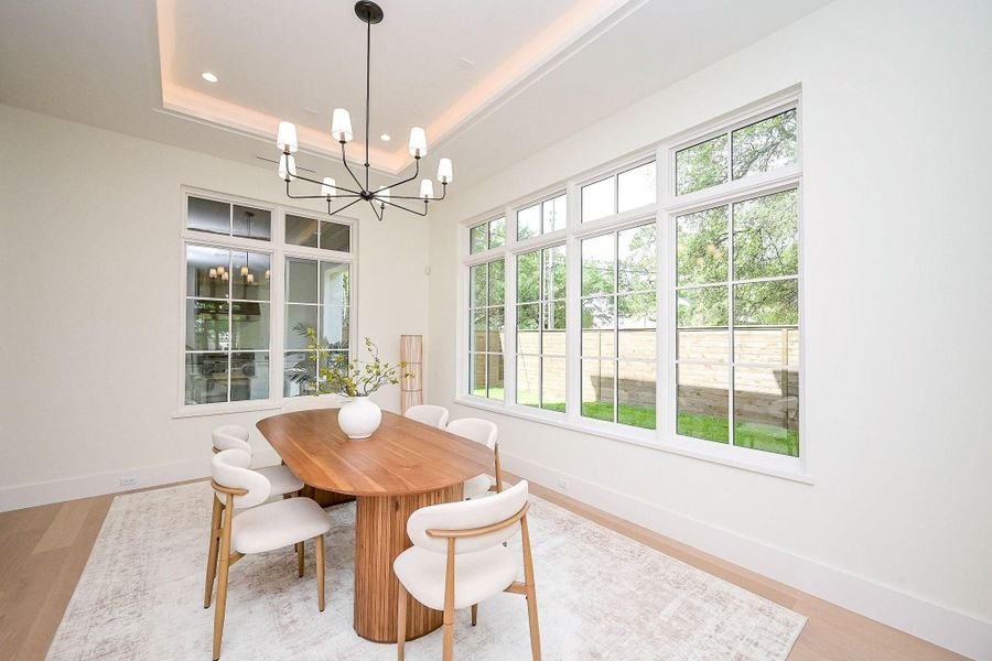 This dining room features large windows offering abundant natural light, a modern chandelier. The neutral color palette and sleek design create a welcoming atmosphere.