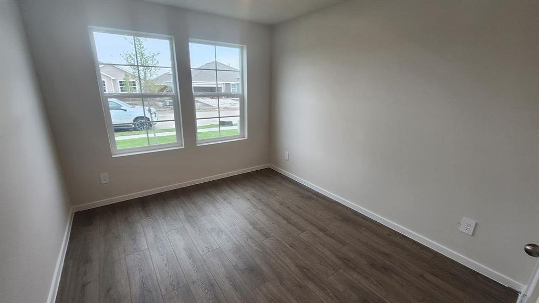 Bright room featuring two windows with white trim, wood-finish flooring, light neutral-toned walls, and white baseboards