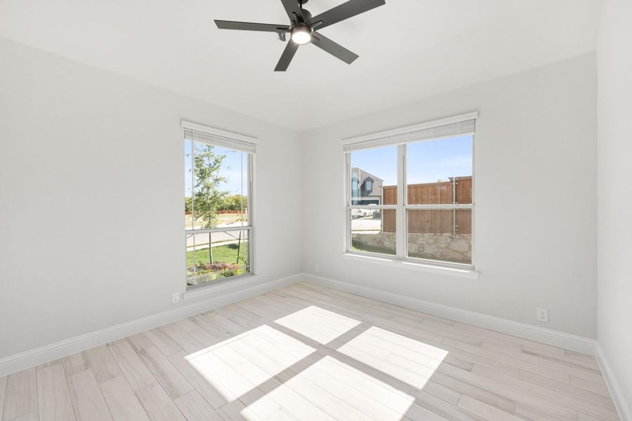 Empty bedroom with light wood floors, ceiling fan, and two windows with backyard views