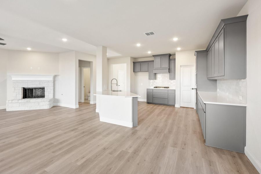 Open-concept kitchen and living area with gray cabinets, white island, light wood floors, and stone fireplace. Open-concept kitchen and living area with gray cabinets, white island, light wood floors, and stone fireplace.