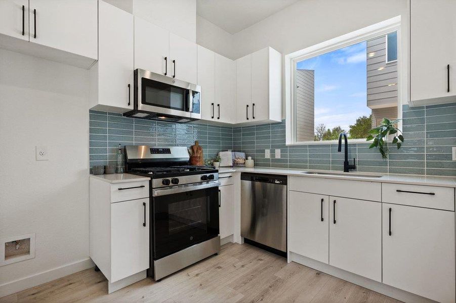 The kitchen features white cabinetry, stainless steel appliances, and a light blue tile backsplash