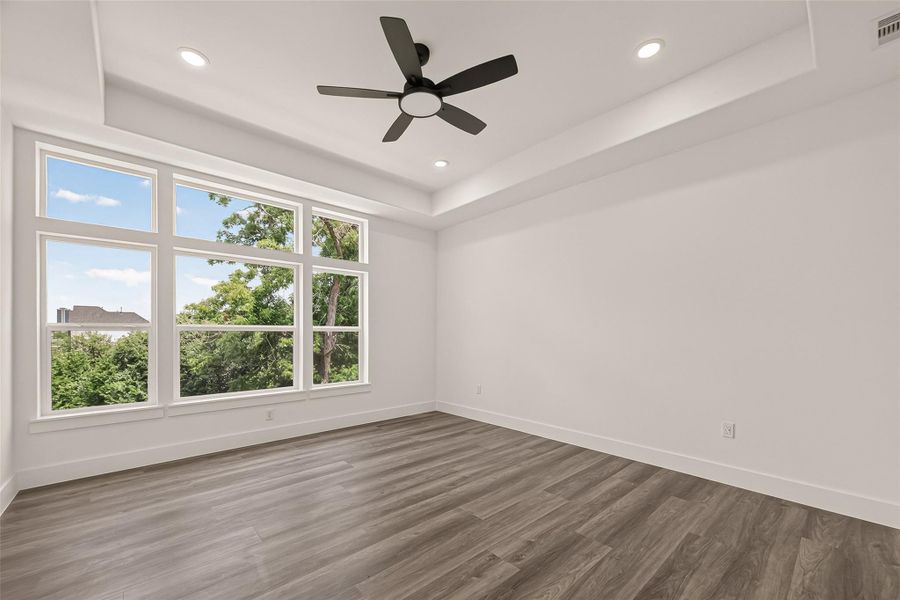 Bright, spacious room with large windows offering a view of greenery. Features include laminate wood flooring, recessed lighting, and a ceiling fan. Ideal for a modern, airy living space. Bright, spacious room with large windows offering a view of greenery. Features include laminate wood flooring, recessed lighting, and a ceiling fan. Ideal for a modern, airy living space.