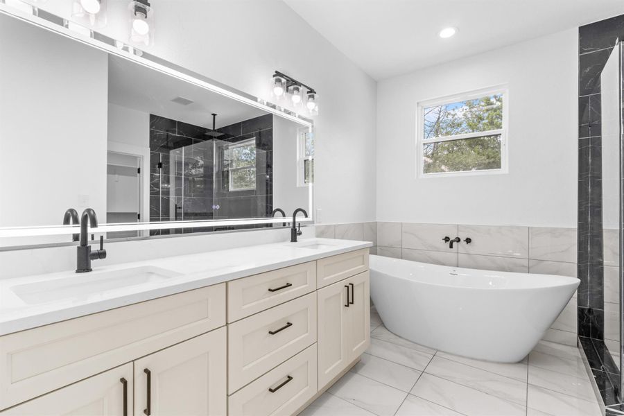 Primary Bath with a walk-in shower, double vanity, a soaking tub, light marble finish flooring, and tile walls