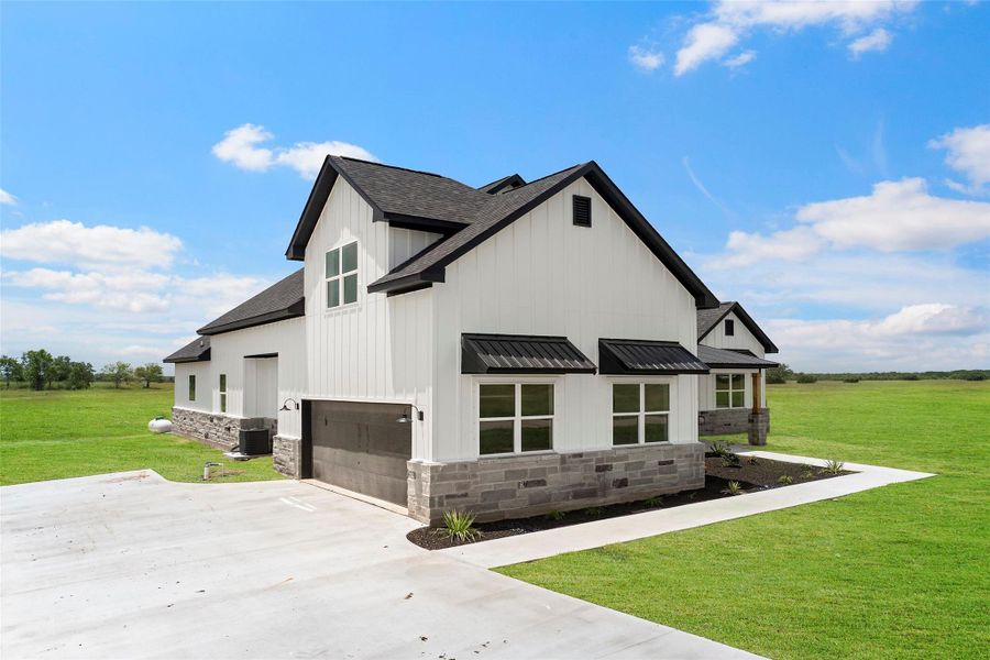 Modern farmhouse with stunning side profile, featuring sleek black accents and expansive windows, surrounded by lush greenery.