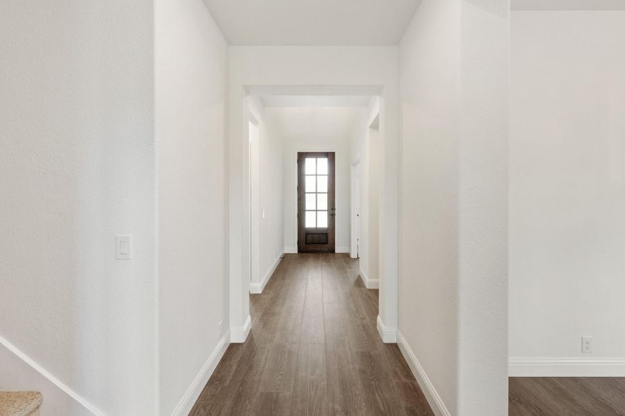 Hallway with white walls, dark hardwood floors, and glass-panel door at the end