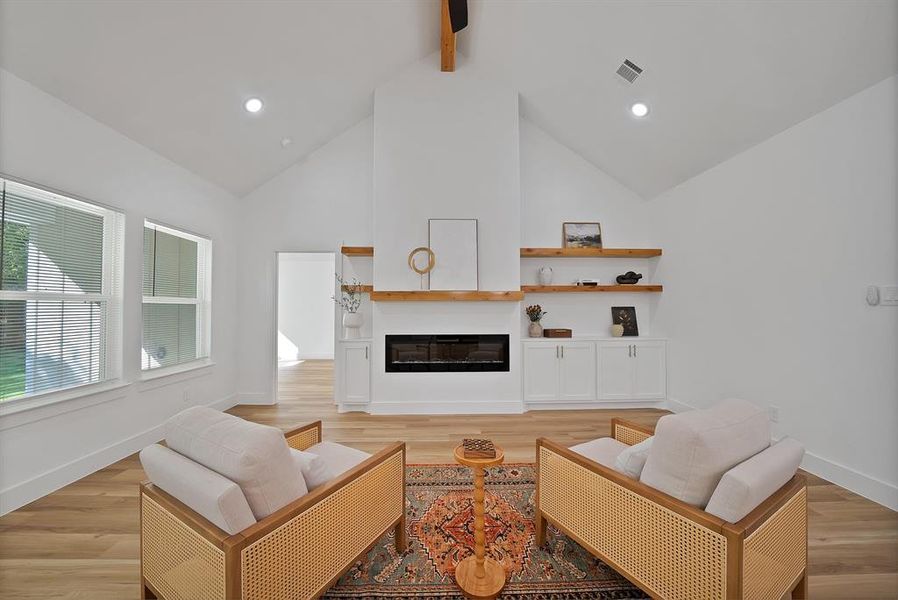 Living room with high vaulted ceiling, light wood-style floors, a glass covered fireplace, beamed ceiling, and recessed lighting