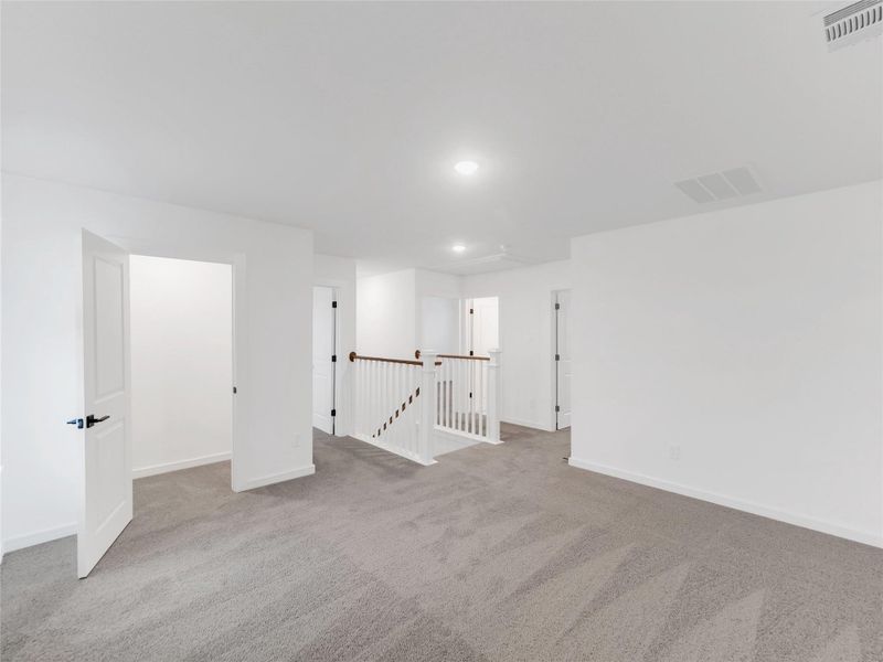 Bright, spacious upstairs area with neutral carpeting, multiple doors leading to separate rooms, and a white railing overlooking the staircase. Ideal for a versatile living space or home office.