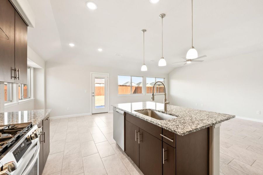 Kitchen with dark brown cabinets, granite island with sink, pendant lights, and stainless steel appliances Kitchen with dark brown cabinets, granite island with sink, pendant lights, and stainless steel appliances