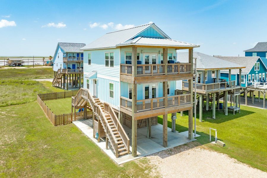 Angled exterior view showcases the home's spacious layout, expansive covered decks, fenced backyard, and elevated construction for coastal convenience.