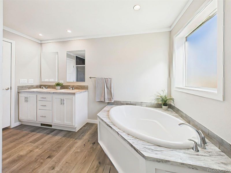 Primary Bath Soaking Tub – An angled view of the deep soaking tub beneath a large frosted window adds to the spa-inspired feel of this relaxing retreat.