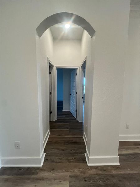 This photo shows a hallway with an arched entryway, leading to multiple rooms. It features white walls, medium gray/wood water proof plank flooring, and modern interior doors, creating a clean and contemporary look.