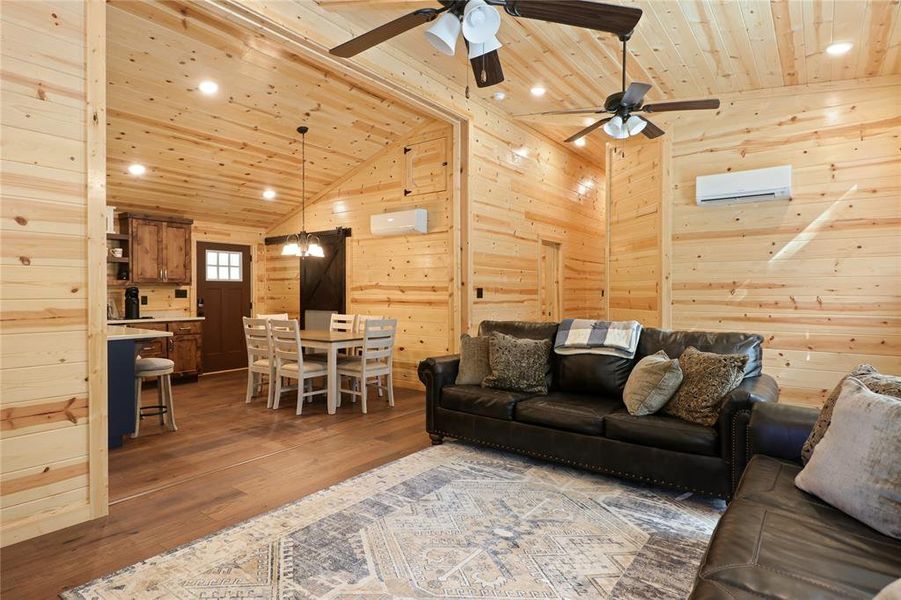 Living room with a wall unit AC, wood walls, ceiling fan, and hardwood / wood-style floors