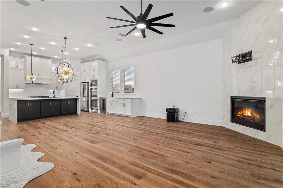 Unfurnished living room with recessed lighting, light wood-style flooring, a fireplace, wine cooler, and a chandelier Unfurnished living room with recessed lighting, light wood-style flooring, a fireplace, wine cooler, and a chandelier