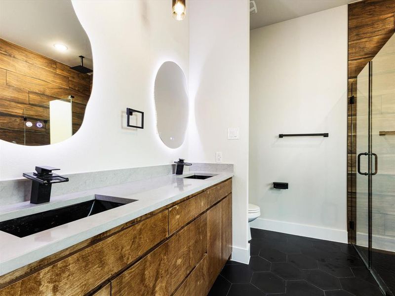 Full bath with double vanity, a shower stall, and dark tile patterned flooring