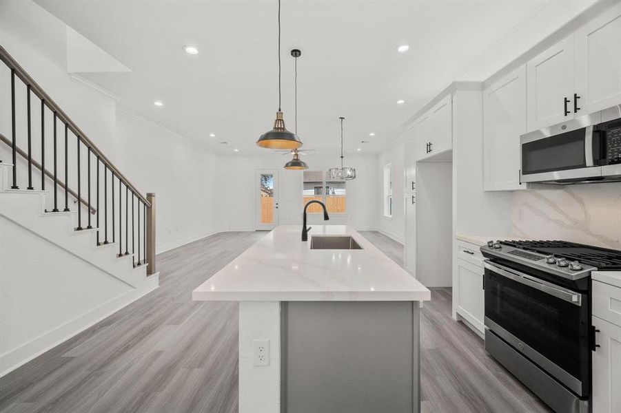 Take a look at the view from the kitchen! It features stunning quartz countertops with elegant backsplashes adorned with a gold inlay. The pendant lights add a touch of sophistication, and let’s not overlook the slow-close cabinets for added convenience.