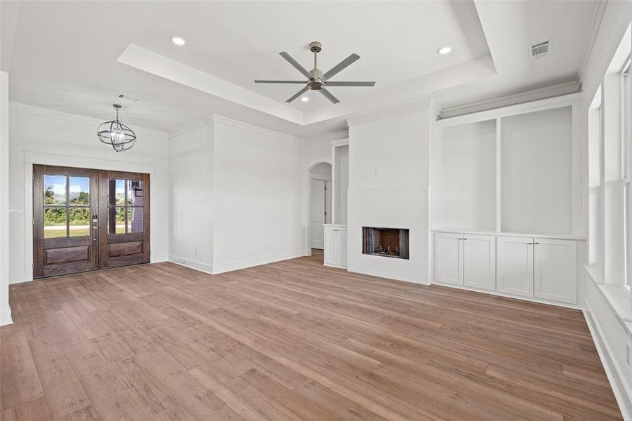 Spacious living area featuring wood-finish flooring, a tray ceiling with recessed lighting, and a modern ceiling fan