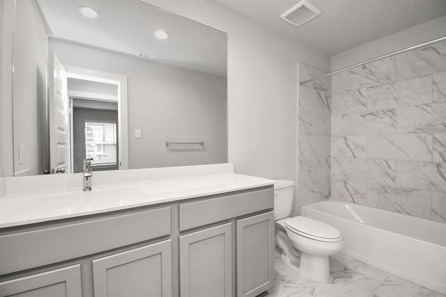 The secondary bath boasts stylish tile flooring, a bath/shower combo with a sleek tile surround, light wood cabinets, and a stunning light countertop. Sample photo of completed home with similar floor plan. Actual colors and selections may vary.