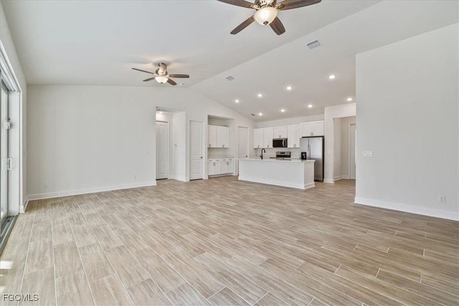 Unfurnished living room with lofted ceiling, wood tiled floors, recessed lighting, and ceiling fan
