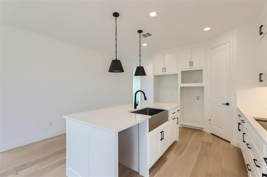 Kitchen featuring hanging light fixtures, light wood-type flooring, a kitchen island with sink, white cabinets, and sink