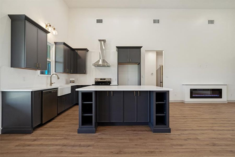 Spacious kitchen featuring dark cabinetry with gold-tone hardware, white countertops, a large center island with integrated shelving, and stainless steel appliances