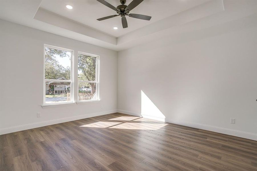 Empty room with a raised ceiling, dark wood-style floors, recessed lighting, and a ceiling fan