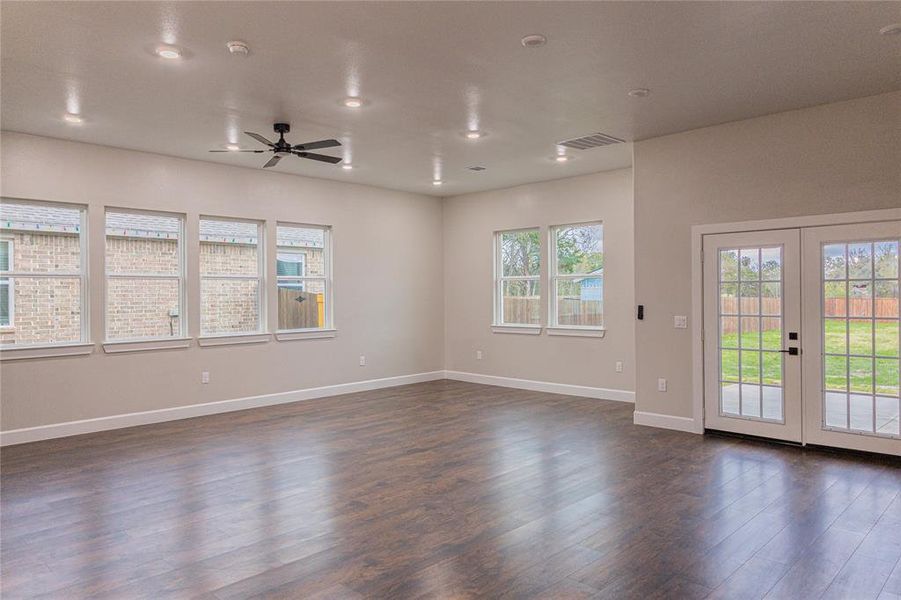 Empty room with plenty of natural light, dark wood-style floors, a ceiling fan, french doors, and recessed lighting Empty room with plenty of natural light, dark wood-style floors, a ceiling fan, french doors, and recessed lighting