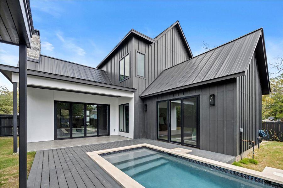 Back of house with board and batten siding, a metal roof, a wooden deck, and a patio area