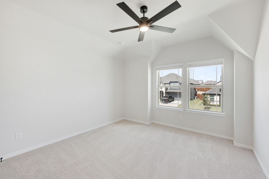 Empty bedroom with vaulted ceiling, ceiling fan, carpet flooring, and double windows overlooking neighborhood