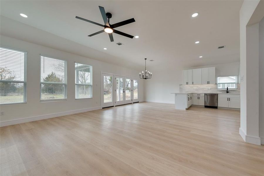 Unfurnished living room featuring ceiling fan with notable chandelier, a healthy amount of sunlight, sink, and light wood-type flooring