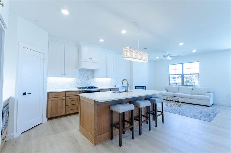 Kitchen featuring two tone color scheme, hanging light fixtures, decorative backsplash, a kitchen island with sink, and a kitchen bar