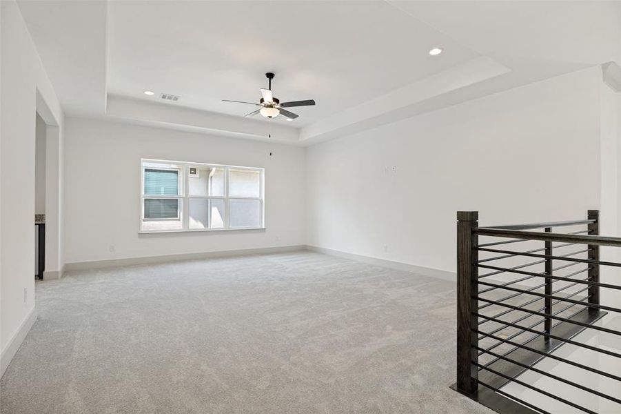 Spacious room featuring light gray carpeting, a tray ceiling with recessed lighting, and a ceiling fan Spacious room featuring light gray carpeting, a tray ceiling with recessed lighting, and a ceiling fan