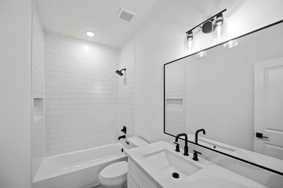 This first level bathroom features a sleek, modern design with white subway tile walls, a built-in bathtub, and a stylish vanity with a large mirror. Black fixtures add a contemporary touch.