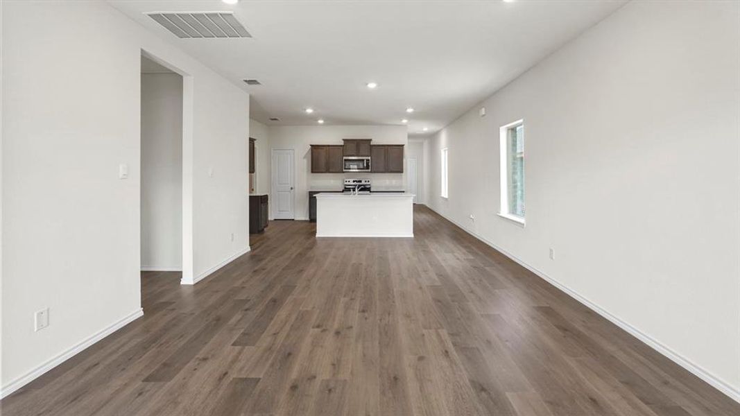 Spacious interior featuring wood-finish flooring, recessed lighting, white walls, multiple windows, and an open-concept kitchen with dark cabinetry and a white island